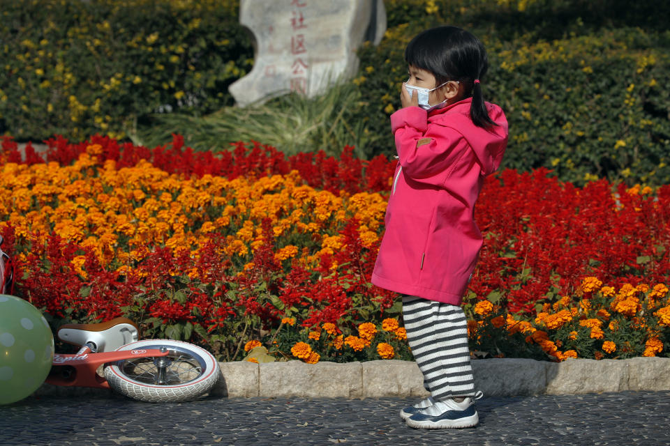 A child holds her face mask to help curb the spread of the coronavirus plays at a park in Beijing, Thursday, Nov. 5, 2020. China is suspending entry for most foreign passport holders who reside in Britain, reacting to a new surge of coronavirus cases in the United Kingdom. (AP Photo/Andy Wong)