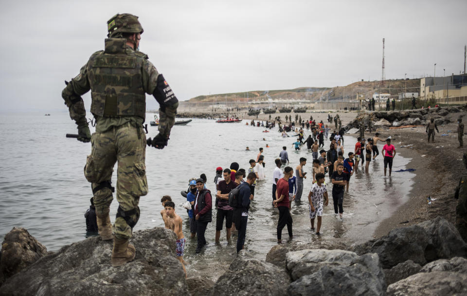 People mainly from Morocco stand on the shore as Spanish Army cordon off the area at the border of Morocco and Spain, at the Spanish enclave of Ceuta, on Tuesday, May 18, 2021. Ceuta, a Spanish city of 85,000 in northern Africa, faces a humanitarian crisis after thousands of Moroccans took advantage of relaxed border control in their country to swim or paddle in inflatable boats into European soil. Around 6,000 people had crossed by Tuesday morning since the first arrivals began in the early hours of Monday, including 1,500 who are presumed to be teenagers. (AP Photo/Javier Fergo)