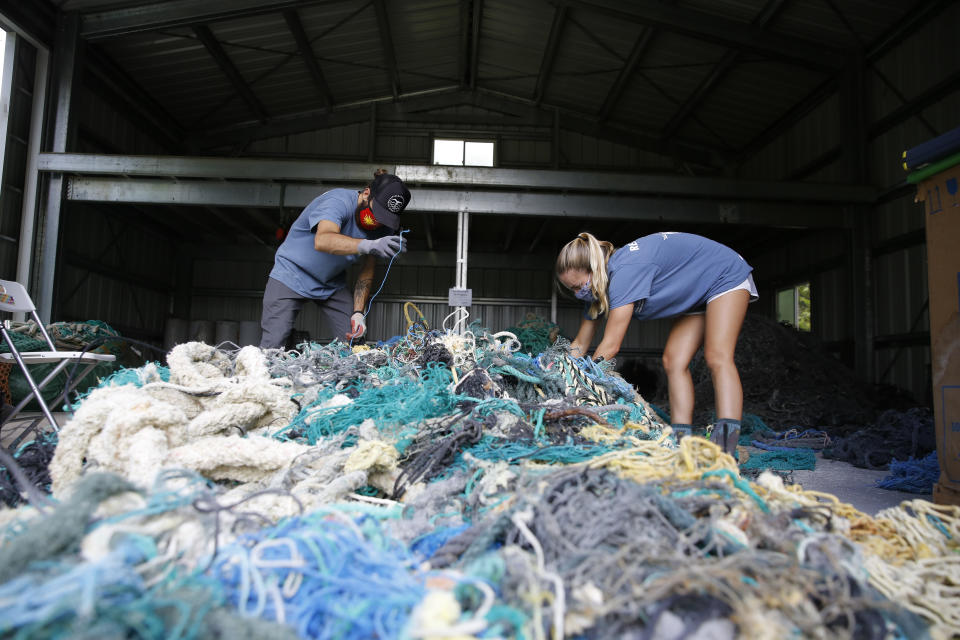 Drew McWhirter (izq) y Raquel Corniuk tratan de desenredar una enorme medeja de redes de pescadores en el Centro de Investigación de Desechos Marinos de la Universidad del Pacífico de Hawái en Kaneohe, Hawái, el 12 de mayo del 2021. (AP Photo/Caleb Jones)