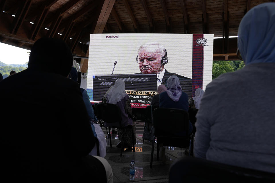 Women from Srebrenica watch a live broadcast from the Yugoslav War Crimes Tribunal in The Hague to learn the verdict for Bosnian Serb military chief Ratko Mladic, on the screen, at the memorial cemetery in Potocari near Srebrenica, eastern Bosnia, Tuesday, June 8, 2021. The United Nations court delivers its verdict in the appeal by former Bosnian Serb military chief Ratko Mladic against his convictions for genocide and other crimes and his life sentence for masterminding atrocities throughout the Bosnian war.(AP Photo/Darko Bandic)