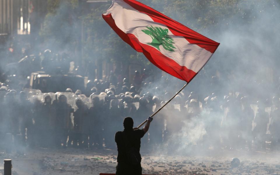 A demonstrator waves the Lebanese flag in front of riot police during a protest in Beirut - REUTERS