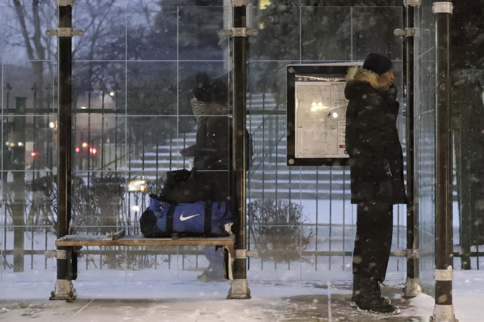 A pedestrian waits for a bus at a bus stop during a snow day in Chicago, Friday, Jan. 17, 2020. Hundreds of flights were canceled as a winter storm hits the city during evening commute Friday, creating a sloppy rush hour. (AP Photo/Nam Y. Huh)