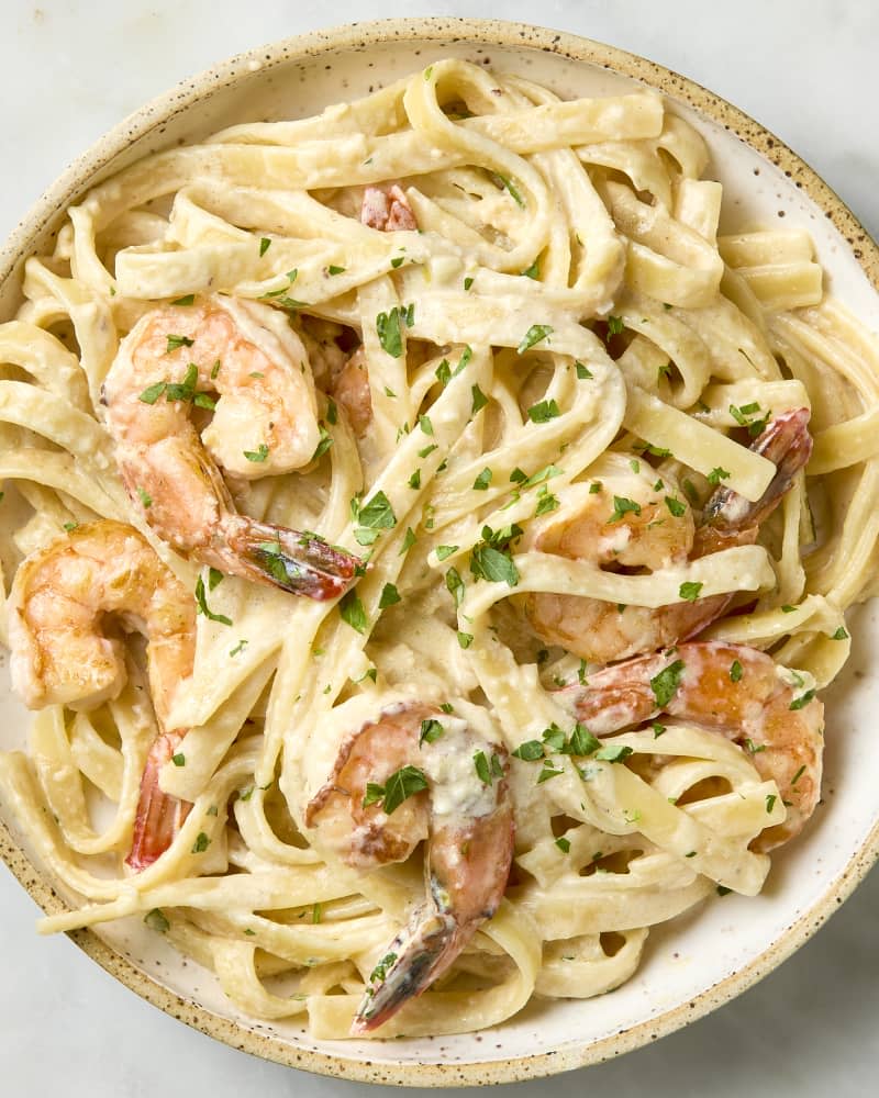 overhead shot of shrimp pasta in a beige bowl, topped with herbs
