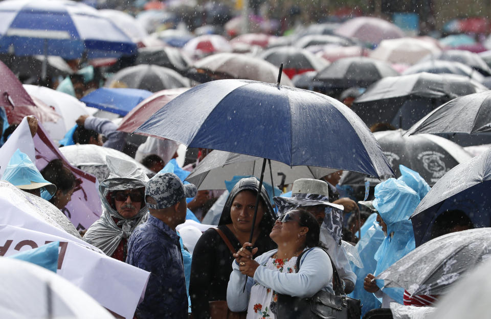 People brave the afternoon rain as they attend a rally on the one-year anniversary of Mexican President Andres Manuel Lopez Obrador's election, in Mexico City's main square, the Zocalo, Monday, July 1, 2019.(AP Photo/Fernando Llano)