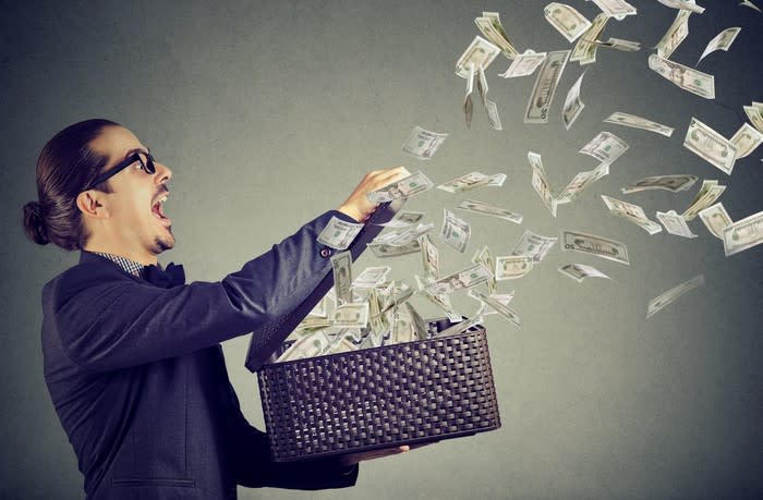 A young man opens a gift box, and dollar bills fly out.