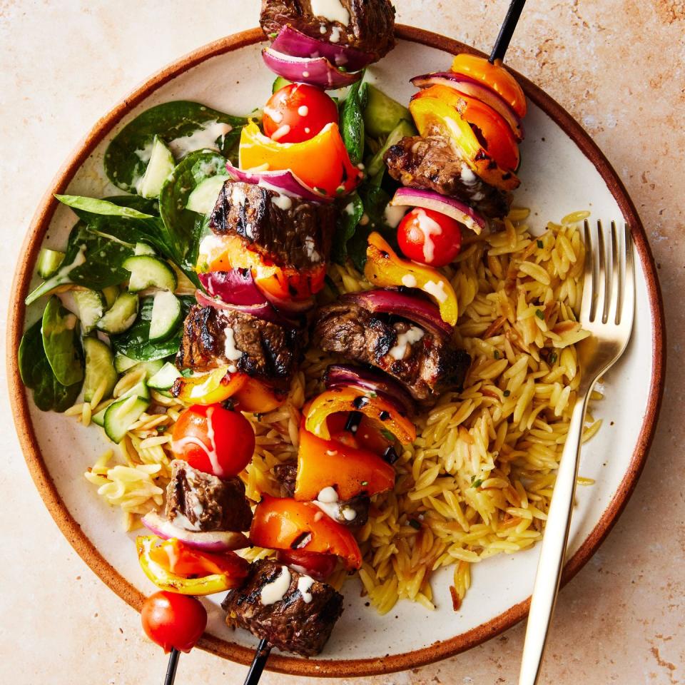 steak kebabs with peppers and tomatoes on top of orzo with a spinach and cucumber salad