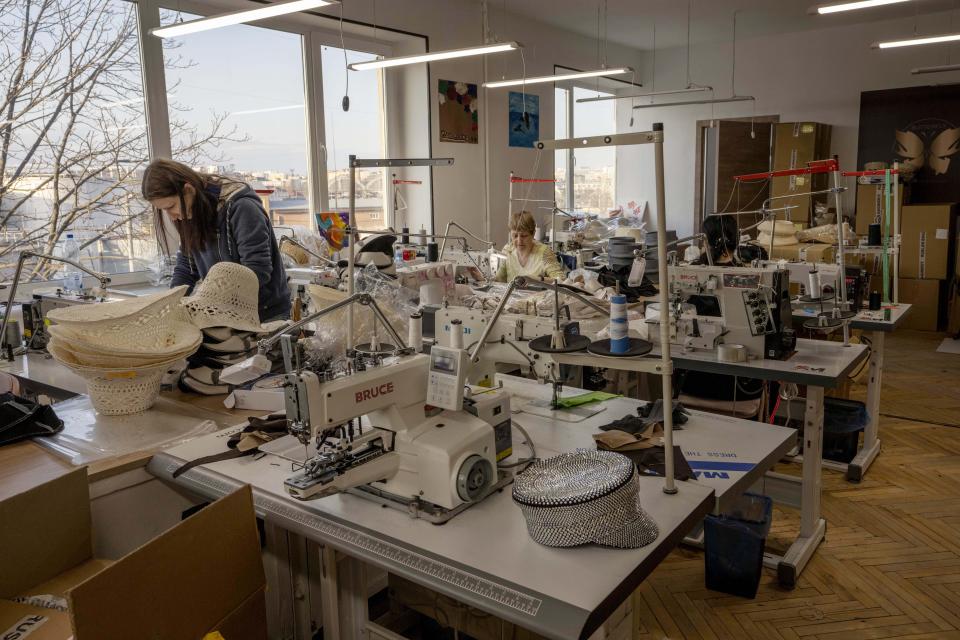 Ukrainian hat makers for high-end designer brand Ruslan Baginskiy 'RB', work inside a college classroom turned into a working space for the company after fleeing Kiev, in Lviv, western Ukraine, Friday, March 25, 2022. The hat with silver stones was worn by American celebrity singer-songwriter Miley Cyrus. (AP Photo/Nariman El-Mofty)