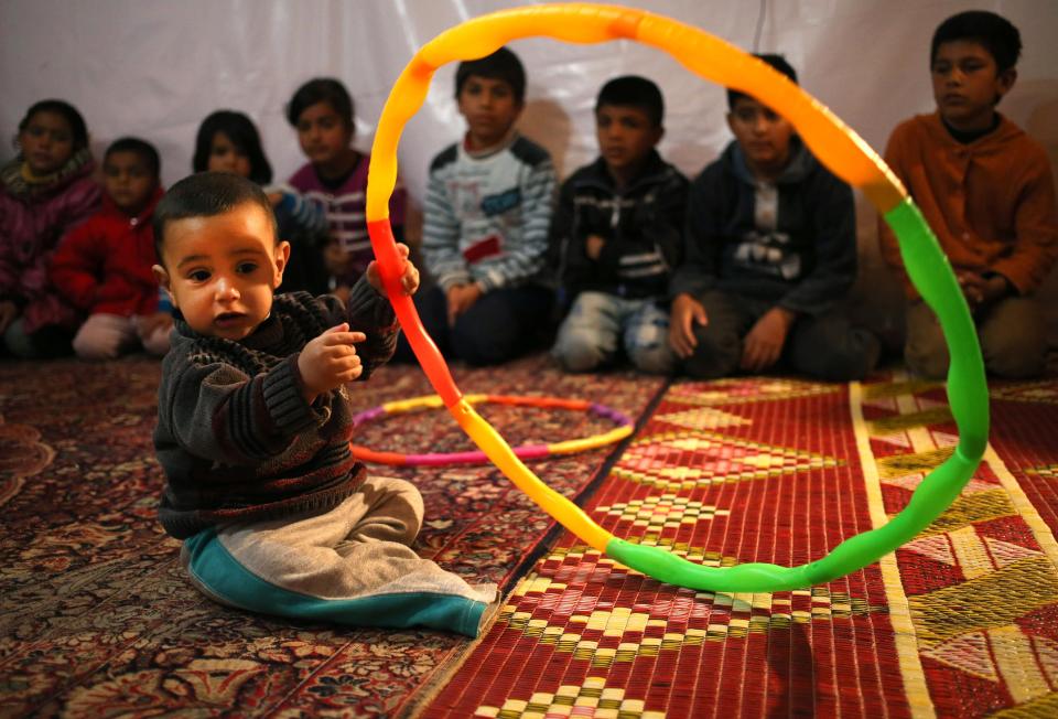 In this picture taken on Wednesday, March 12, 2014, a Syrian refugee child Hisham al-Sahou, 1, plays with hula hoop as he sits in front of Syrian refugee students, background, who listen for a story read by their teacher inside a tent a home for a refugee family that turns into a makeshift school in a refugee encampment in the Lebanese-Syrian border town of Majdal Anjar, eastern Bekaa valley, Lebanon. More than 2 million of those who should be in school remain in Syria, where classrooms have been bombed, used as shelters or turned into military barracks. Another 300,000 Syrian children don’t attend school in Lebanon, along with some 93,000 in Jordan, 78,000 in Turkey, 26,000 in Iraq and 4,000 in Egypt, UNICEF officials in Geneva said. Those numbers likely are higher, as UNICEF can’t count the children whose parents didn’t register with the United Nations refugee agency. (AP Photo/Hussein Malla)