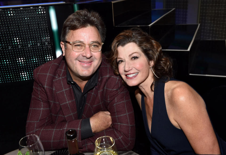 Vince Gill in a burgundy plaid suit with Amy Grant leaning on him, wearing a black dress