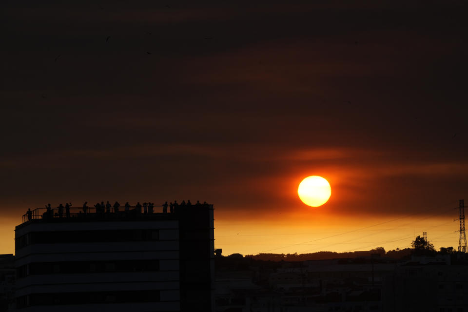 The sun sets over people waiting on top of a building for the start of a vigil with Pope Francis at the Parque Tejo in Lisbon, Saturday, Aug. 5, 2023, ahead of the 37th World Youth Day. On Sunday morning, the last day of his five-day trip to Portugal, Francis is to preside over a final, outdoor Mass on World Youth Day – when temperatures in Lisbon are expected to top 40 degrees C (104F) – before returning to the Vatican. (AP Photo/Gregorio Borgia)