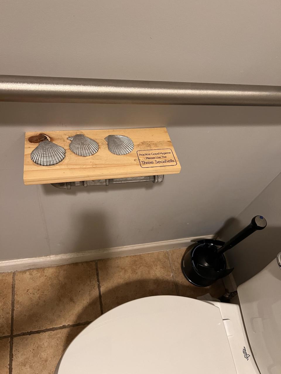Wooden shelf in bathroom with three seashells and text: "Please Consider Using These Seashells."