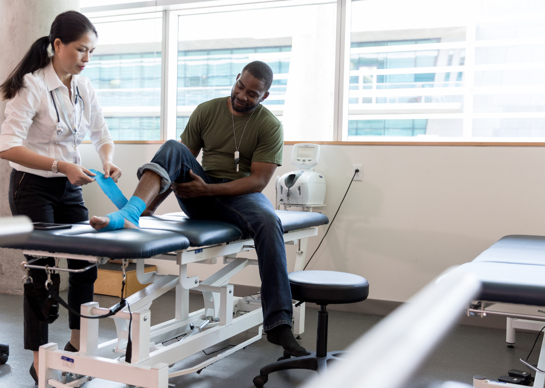 A physical therapist helps a man unwrap a bandaged leg.