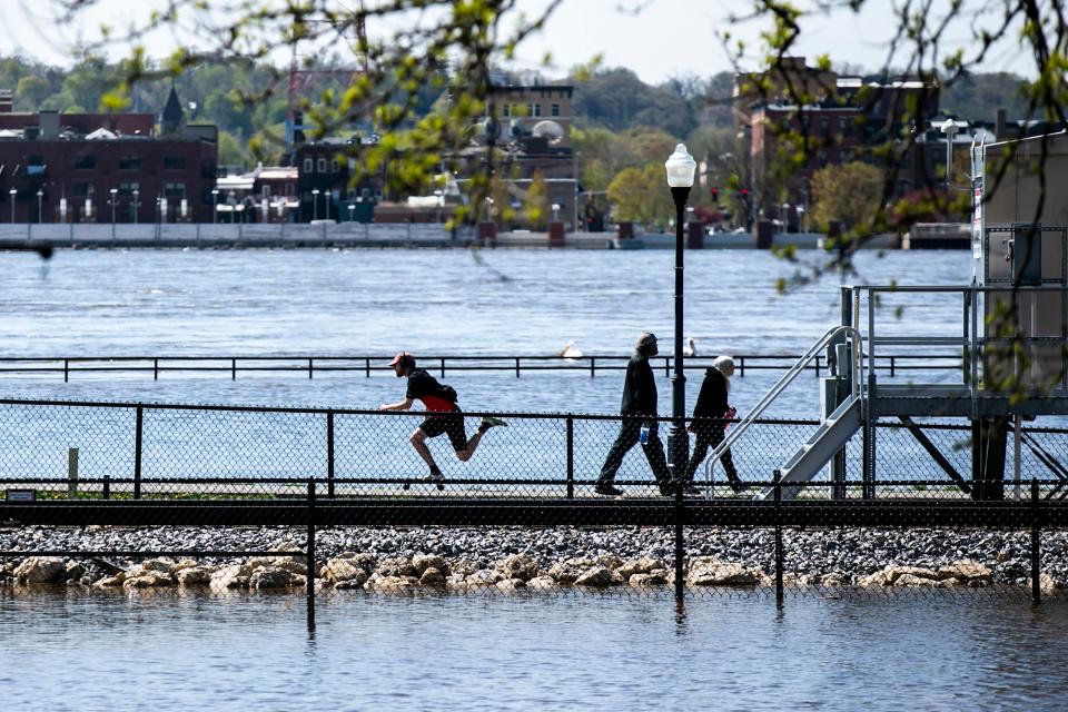 People walk along a path way between water from the Mississippi River that is out of its banks over River Drive during a river flood warning, Wednesday, April 26, 2023, in Davenport, Iowa.