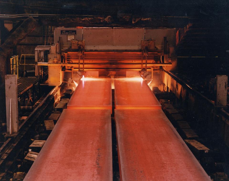 Hot steel coming out of a forging oven in two long strips.