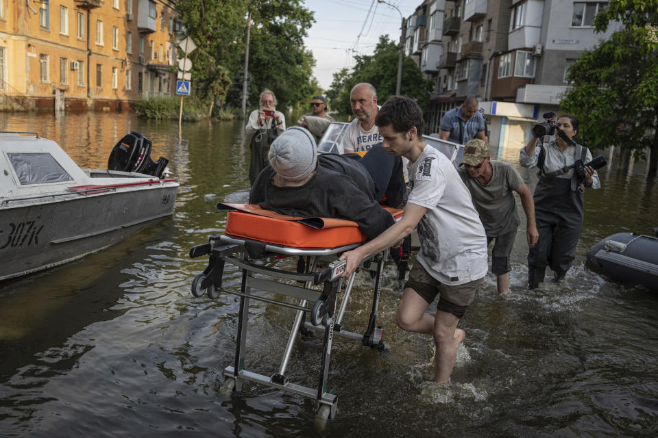 FILE - Volunteers haul a woman on a stretcher as she been evacuated from a flooded neighborhood of the left bank Dnipro river, in Kherson, Ukraine, Friday, June 9, 2023. In Ukraine, the governor of the Kherson region, Oleksandr Prokudin, said Friday that water levels had decreased by about 20 centimeters (8 inches) overnight on the western bank of the Dnieper, which was inundated starting Tuesday after the breach of the Nova Kakhovka dam upstream. (AP Photo/Evgeniy Maloletka, File)