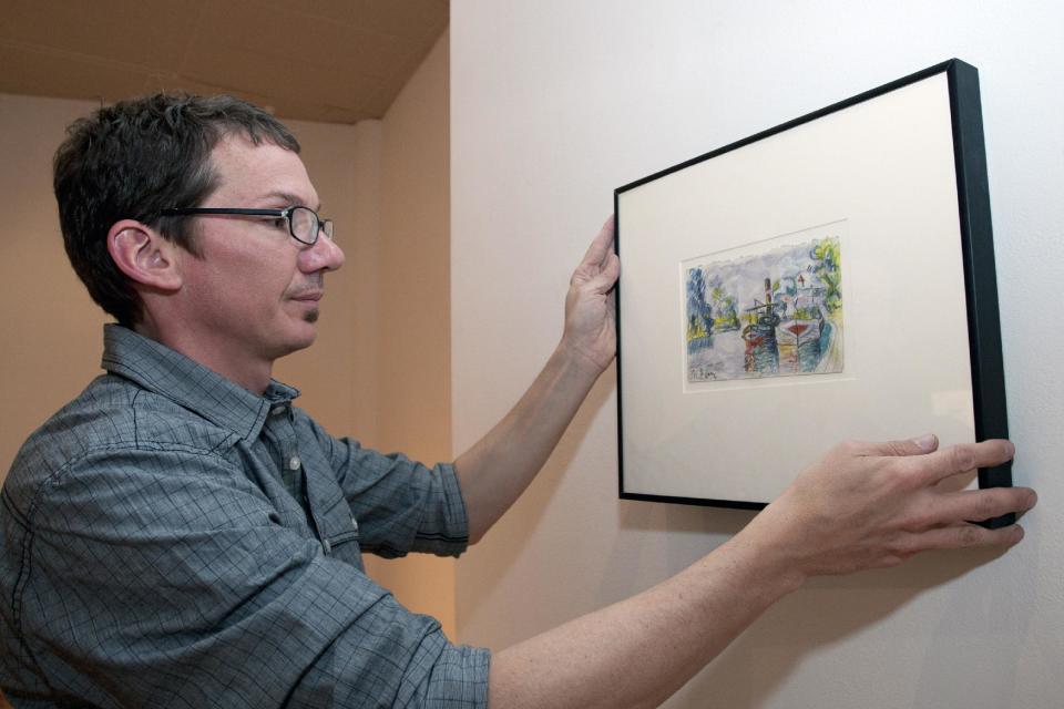 Director of DAAP Galleries at the University of Cincinnati, Aaron Cowan hangs a piece of art by art forger Mark A. Landis, of Laurel, Miss. for a show called "Faux Real" in Cincinnati, Ohio on Tuesday, March 27, 2012. The work of the convincing art forger who has spent nearly three decades copying artists like Picasso and donating his fake art to unsuspecting museums goes on display April Fool's Day. The University of Cincinnati exhibit will explore the problem of art forgery through a look at the unusual story of Landis. (AP Photo/Dottie Stover-University of Cincinnati)