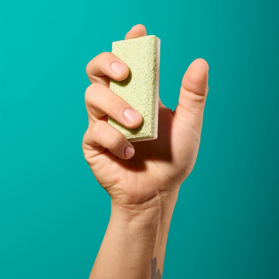 Hand squeezing a green pumice stone against a solid teal background