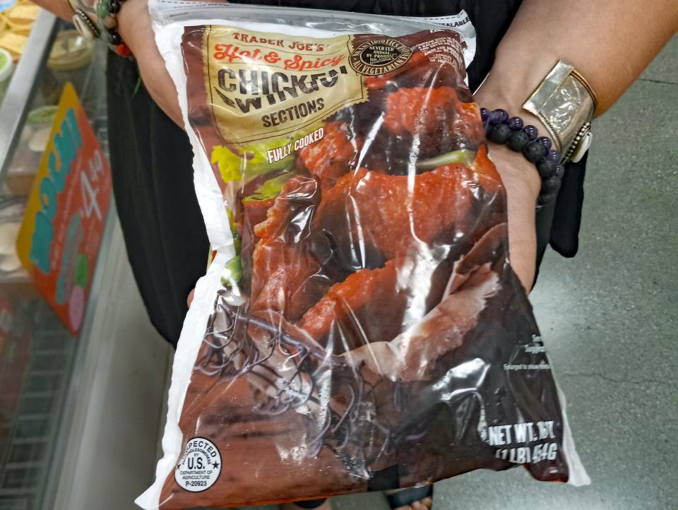 hands holding bag of frozen chicken wings in the freezer aisle of trader joes