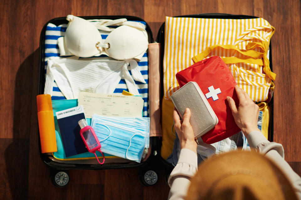 Upper view of modern female with sanitizer, trolley bag, air tickets, medical mask, straw hat, spf, first aid kit and bikini packing trolley bag in the modern house in sunny day.