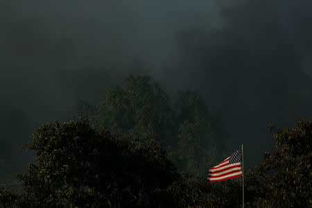 A home burns to the ground as its U.S. flag blows in the wind while the Lilac Fire burns through Bonsall, California, U.S., December 7, 2017. REUTERS/Mike Blake