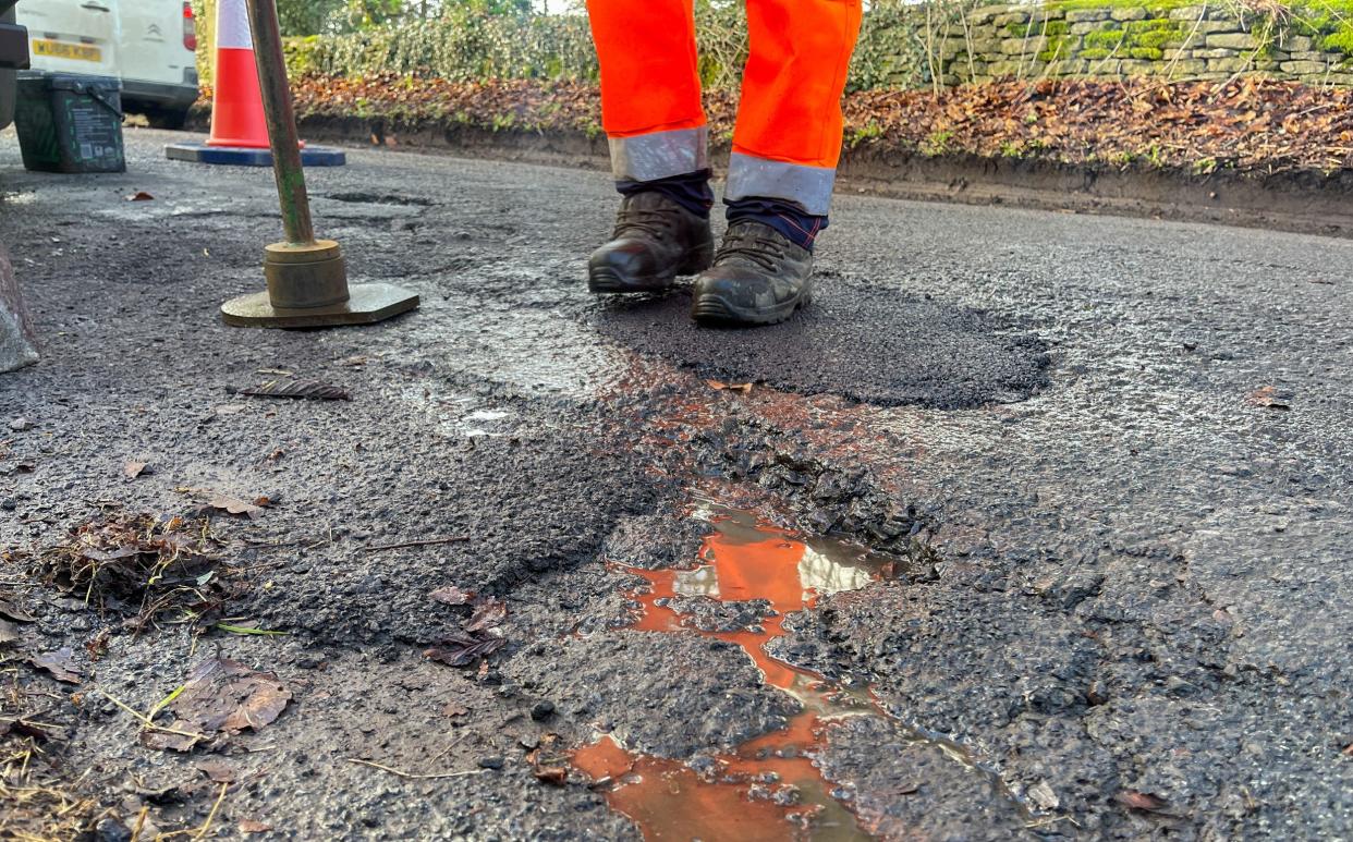 A highway maintenance worker stands next to a pot hole that is about to be repaired