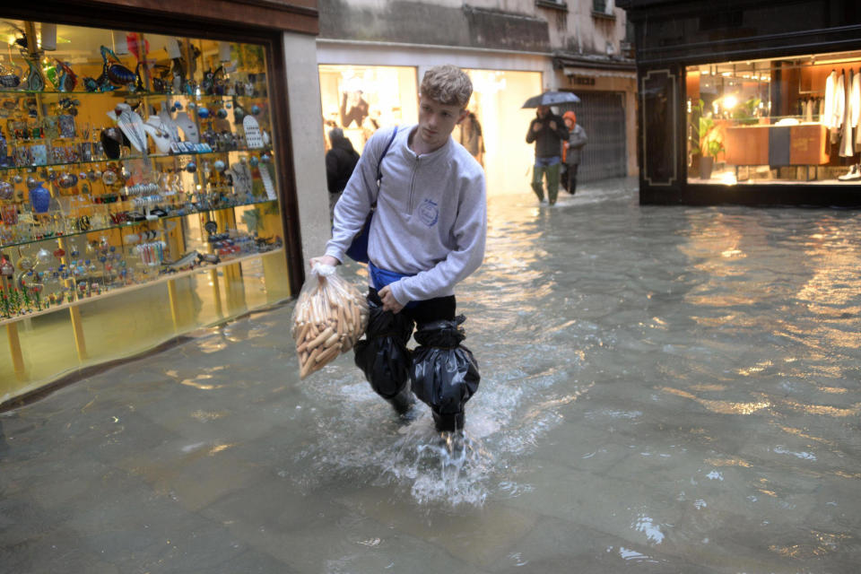 A man holding a bag of what appear to be breadsticks wades through water, in Venice, northern Italy, Friday, Nov. 15, 2019. Exceptionally high tidal waters returned to Venice on Friday, prompting the mayor to close the iconic St. Mark’s Square and call for donations to repair the Italian lagoon city just three days after it experienced its worst flooding in 50 years. (Andrea Merola/ANSA via AP)