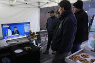 Farmers watch French President Emmanuel Macron speaking at the European Union summit on a blocked highway, Thursday, Feb.1, 2024 in Argenteuil, north of Paris. France's two major farmers unions announced Thursday their decision to suspend protests and lift road blockades across the country. Farmers have been protesting for days across the country to denounce low wages, heavy regulation and unfair competition from abroad. (AP Photo/Michel Euler)