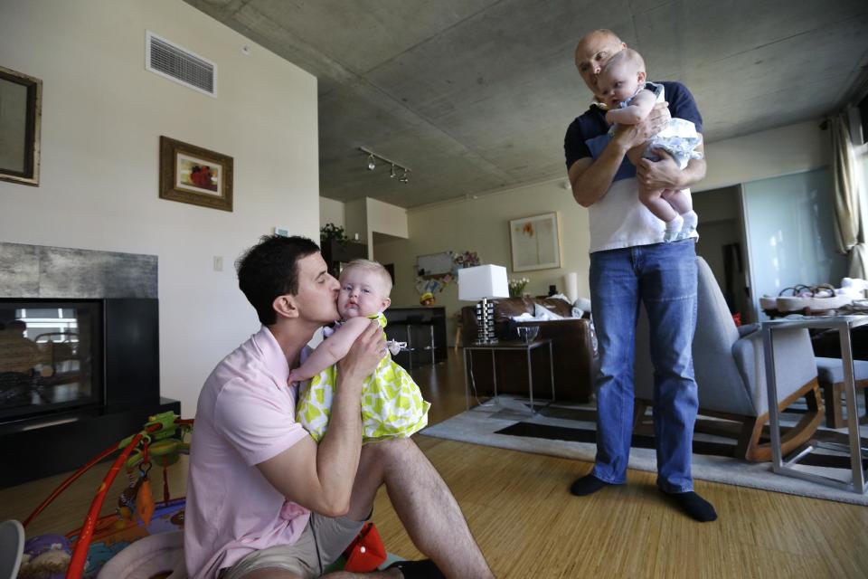 In this Tuesday, Aug. 20, 2013 photo, Trey Powell, left, kisses his daughter, Ashton, as nanny Randy Hambley holds her twin sister, Kylan, in Powell's home in Seattle. Powell says fatherhood is the focus of his life - a transformation made easier because he often works from home and can afford a full-time nanny. (AP Photo/Elaine Thompson)