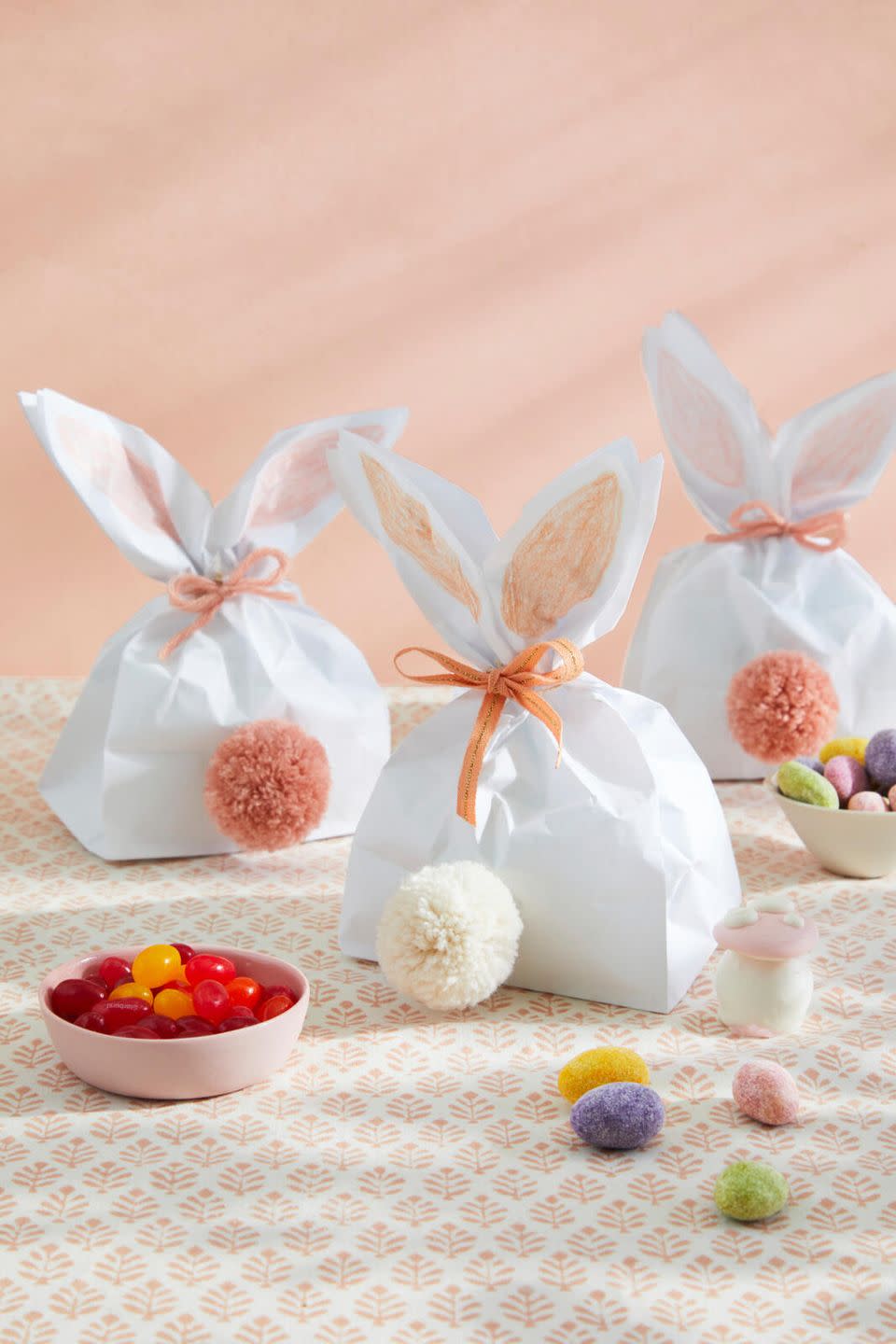 white paper bags that have been trimmed at the top and scrunched at the top and tied so that they look like bunny ears with a pom pom tail at the bottom of the bag