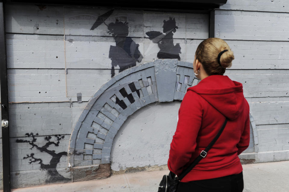 A woman looks at work by British graffiti artist Banksy on Saturday, Oct. 19, 2013 in the Brooklyn borough of New York. The building owner has hired security guards and installed a metal gate to protect a work by Banksy. Cara Tabachnick, whose family owns the building, said the goal is to preserve the artwork "so it can be viewed and enjoyed." Most of the Banksy works that have gone up have been tagged over by others, and some have been completely erased. Mayor Michael Bloomberg said last week that graffiti ruins property and is "a sign of decay." (AP Photo/Alyssa Goodman)