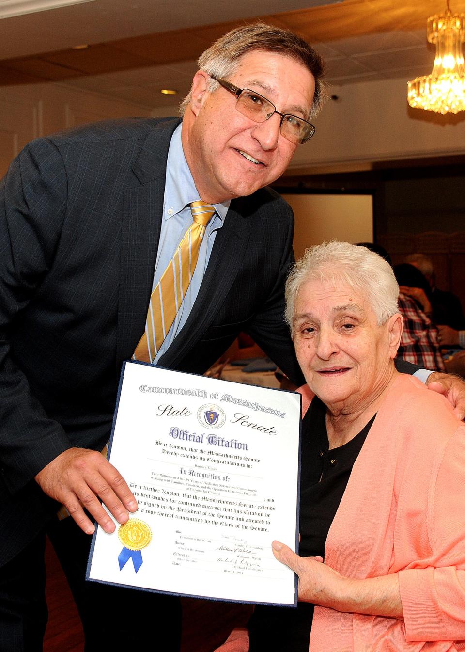 Mass Senator Mike Rodrigues gives a state citation to Barbara Travis during her retirement party.