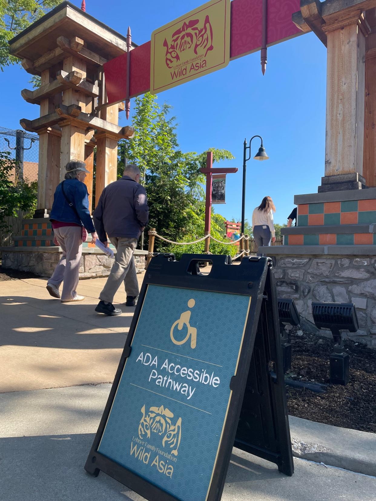 Akron Zoo visitors walk past a sign designating an Americans With Disabilities Act accessible pathway.