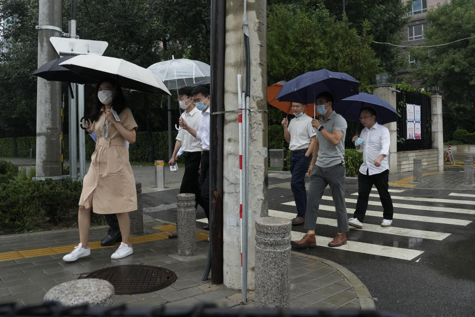 Office workers walk with umbrellas during a rainy day in Beijing, Thursday, Aug. 18, 2022. Some were killed with others missing after a flash flood in western China Thursday, as China faces both summer rains and severe heat and drought in different parts of the country. (AP Photo/Ng Han Guan)