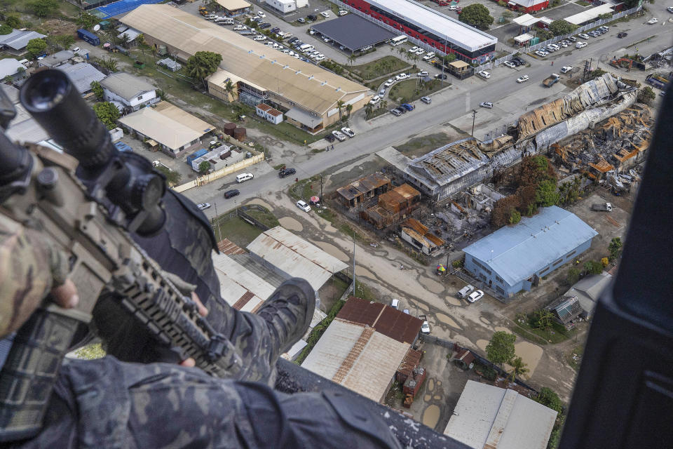 Australian Federal Police Tactical Response officer inspects the damage over the Chinatown area from the air during an operation in Honiara, Solomon Islands, Wednesday, Dec. 1, 2021. New Zealand announced Wednesday that they will send up to 65 military and police personnel to the Solomon Islands over the coming days after rioting and looting broke out there last week. (Gary Ramage via AP)