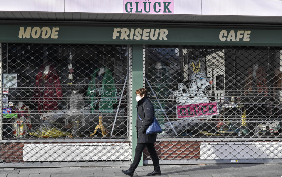 A woman with a face mask passes a closed combined cafe, barber and fashion shop named Glueck (luck) in Duisburg, Germany, Monday, Jan. 25, 2021. (AP Photo/Martin Meissner)