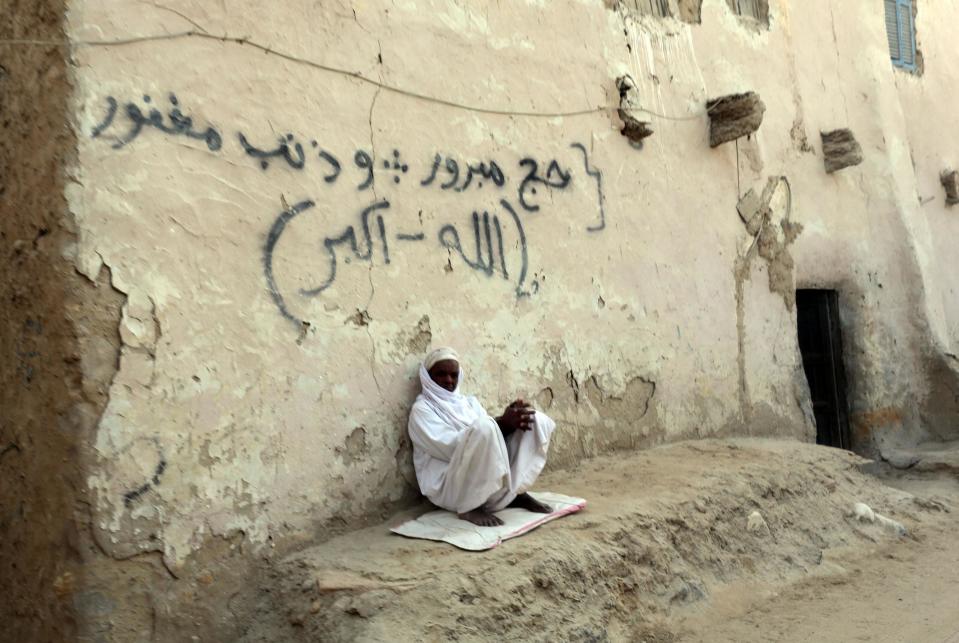 A man sits outside his home in Siwa under graffiti that reads 'May God accept your pilgrimage and forgive your sins' - an expression used for people returning from Mecca