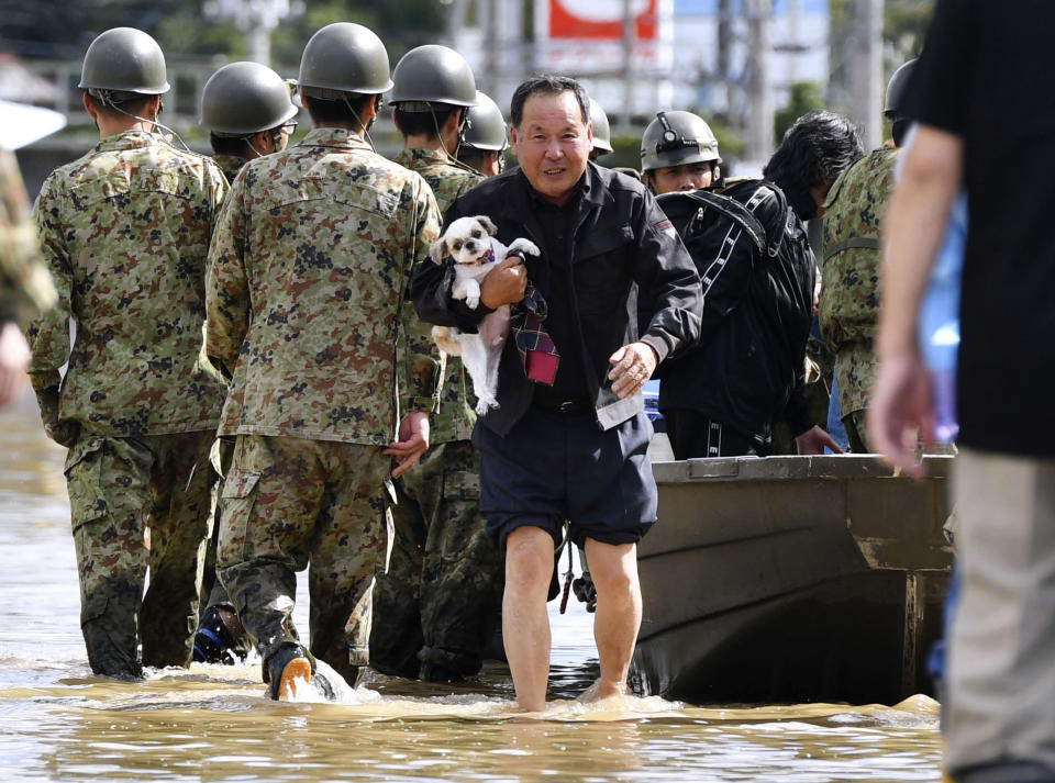 An evacuee with a dog is rescued by Self-Defense force members as the city is hit by Typhoon Hagibis, in Motomiya, Fukushima prefecture, northern Japan, Sunday, Oct. 13, 2019. Rescue efforts for people stranded in flooded areas are in full force after a powerful typhoon dashed heavy rainfall and winds through a widespread area of Japan, including Tokyo.(Kyodo News via AP)