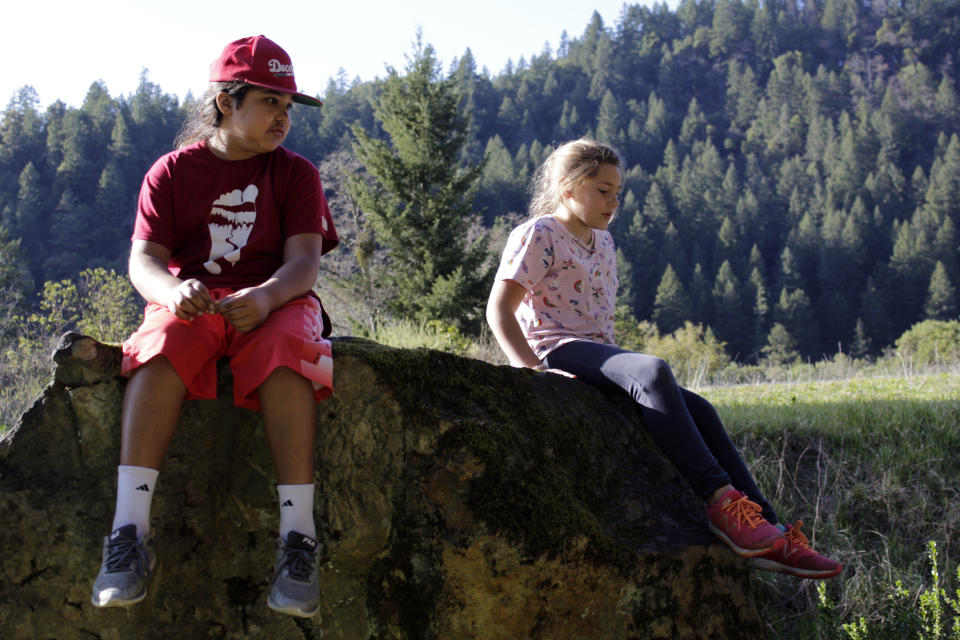 Ishikiihara E-kor plays with his younger sister, Vuunsip Imkuukirii, on rocks near the Karuk Tribal Administration headquarters in the unincorporated community of Orleans in Humboldt County, Calif., on March 4, 2020. Ishikiihara, whose name means sturgeon warrior in the Karuk language, is one of 5,000 members of the Karuk tribe still living in a remote area of far northern California. Ishikiihara has been doing distance learning and has been coping with the pandemic by writing rap songs, one of his favorite hobbies. He celebrated his recent 11th birthday with relatives on a video conference call. (AP Photo/Gillian Flaccus)