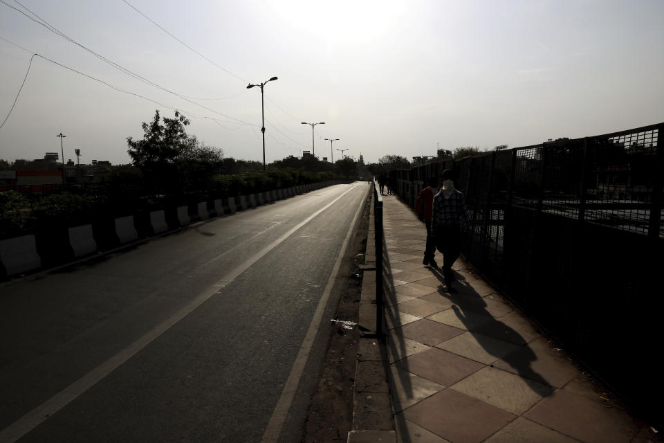 Indians walk wearing face masks on the side of an empty street during a lockdown amid concerns over the spread of Coronavirus, in New Delhi, India, Monday, March 23, 2020. Authorities have gradually started to shutdown much of the country of 1.3 billion people to contain the outbreak. For most people, the new coronavirus causes only mild or moderate symptoms. For some it can cause more severe illness. (AP Photo/Manish Swarup)