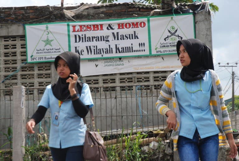 Indonesian Muslim women walking past a banner saying 'homosexual and lesbian banned from entering our neighborhood' in Bandung, West Java province