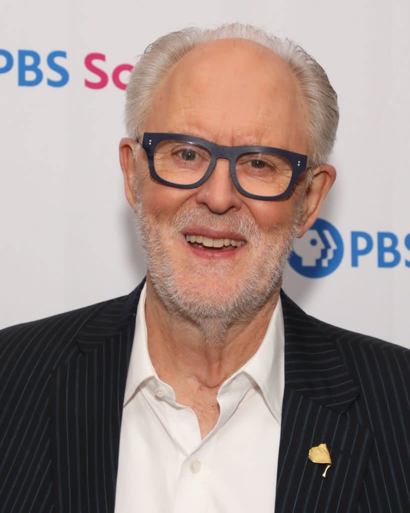 John Lithgow smiles at a PBS promotional event, wearing a striped suit jacket and a white shirt