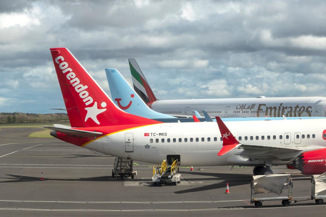 Three airplanes from different airlines, Corendon, TUI, and Emirates, are parked atmanchester  airport gate on a cloudy day.