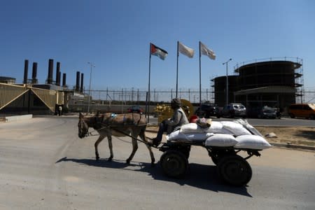 Palestinian man rides a donkey-drawn cart past the Gaza power plant, in the central Gaza Strip