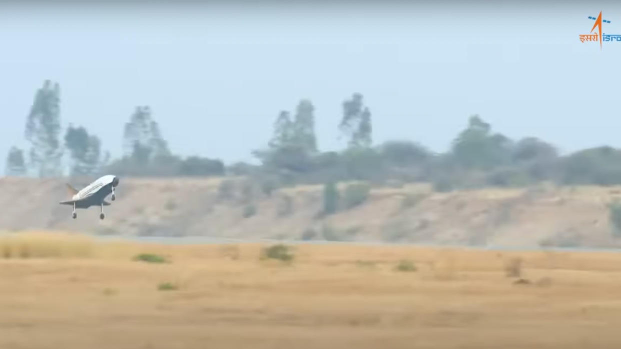  A small space plane comes in for a landing with brown hills in the background. 