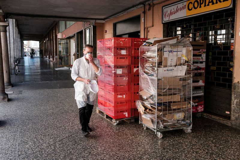 FILE PHOTO: A supermarket worker adjusts a protective face mask as he walks past shops in Casalpusterlengo