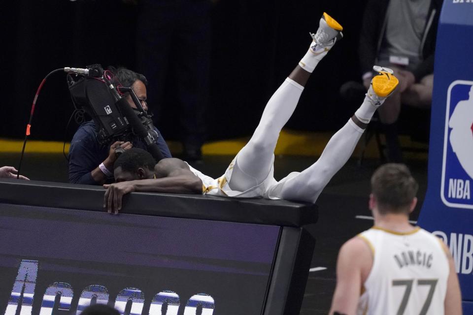 A camera operator moves away as Dallas Mavericks' Dorian Finney-Smith, falls over signage near base court during play as guard Luka Doncic (77) looks on in the second half of an NBA basketball game against the Brooklyn Nets in Dallas, Thursday, May 6, 2021. (AP Photo/Tony Gutierrez)