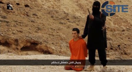 A masked, black-clad militant, who has been identified by the Washington Post newspaper as a Briton named Mohammed Emwazi, stands next to a man purported to be Kenji Goto in this still image from a video obtained from SITE Intel Group website February 26, 2015. REUTERS/SITE Intel Group via Reuters TV