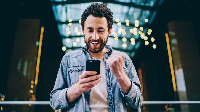 Excited bearded young man blogger cheering favourite team during live stream on website on modern smartphone.