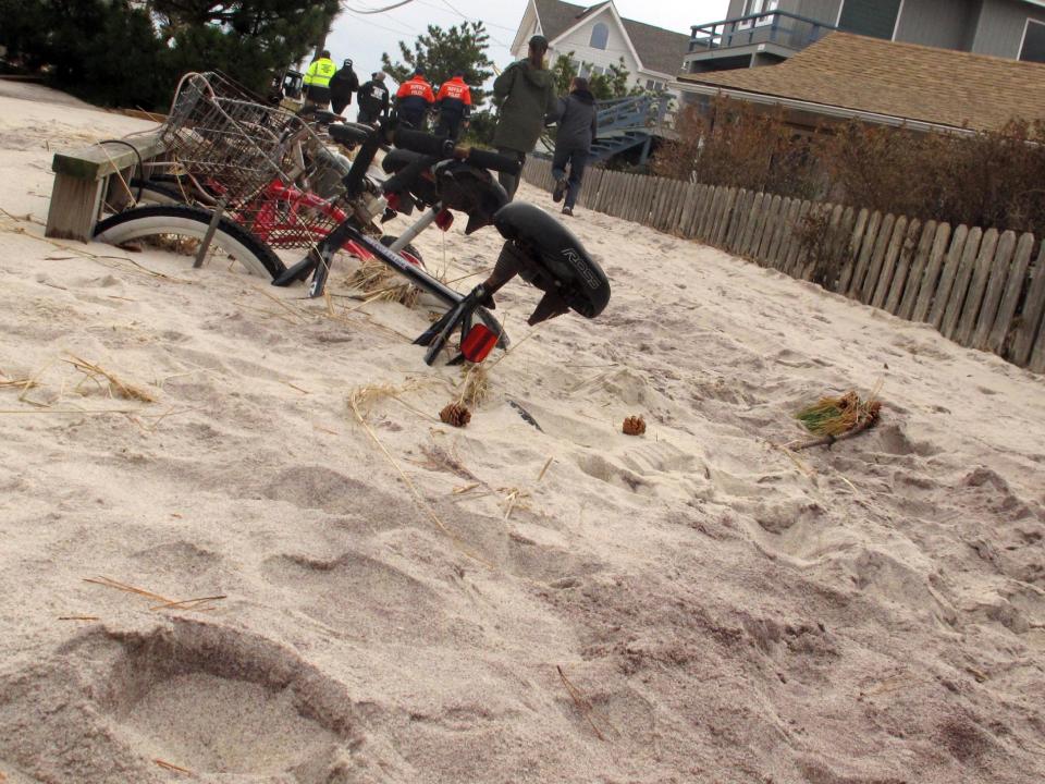 In this Friday, Nov. 16, 2012 photo, bicycles remain buried beneath several feet of sand in the Fire Island community of Kismet, N.Y. In the background, Suffolk County and other officials tour the community damaged from Superstorm Sandy. (AP Photo/Frank Eltman)