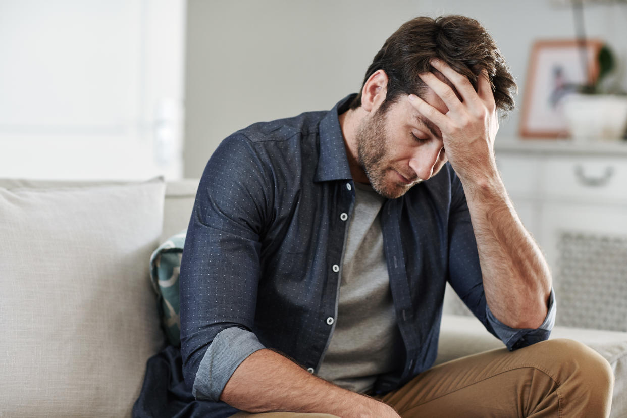 Man looking depressed while sitting alone with his head in his hand on his living room sofa at home after divorce